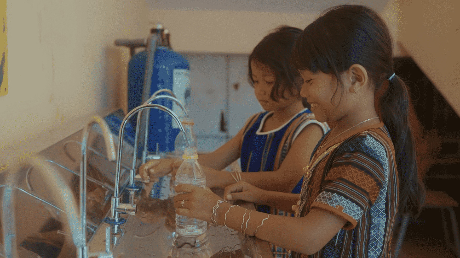 A few young girls filling a bottle of waterDescription automatically generated
